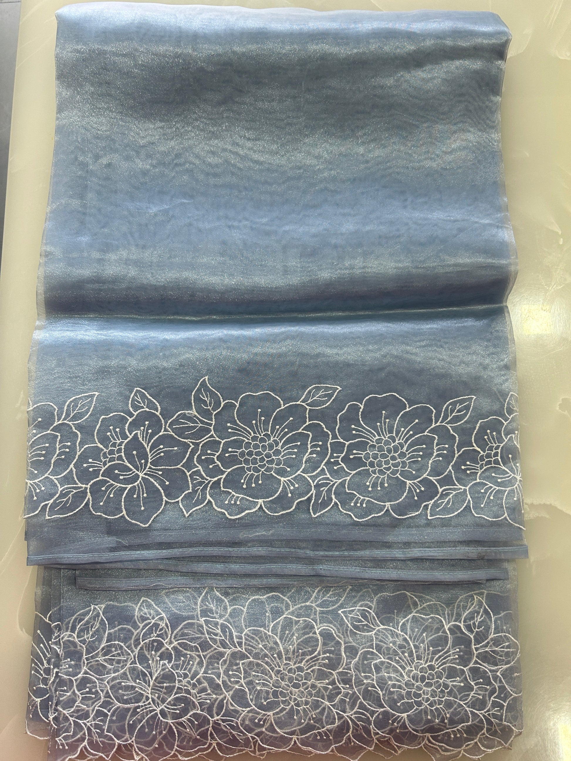 Powder blue tissue silk organza saree with floral cutwork embroidery on the border and a plain body, accompanied by a plain blouse piece.
